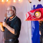 Barnaby Evans, WaterFire creator and Executive Artistic Director/coCEO of WaterFire Providence, speaks at the Olneyville Expo in 2019. Barnaby is seen on stage along with one of our LED illuminated Japanese Koi fish. Photograph by Matthew Huang