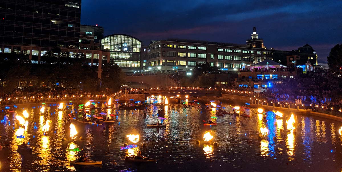 A view of the Basin in Waterplace Park shot during the 2019 Clear Currents Community Paddling Event. Kayaks with Illuminated Koi fish attached circle the ring of braziers in the Basin. Photograph by Tim Blankenship