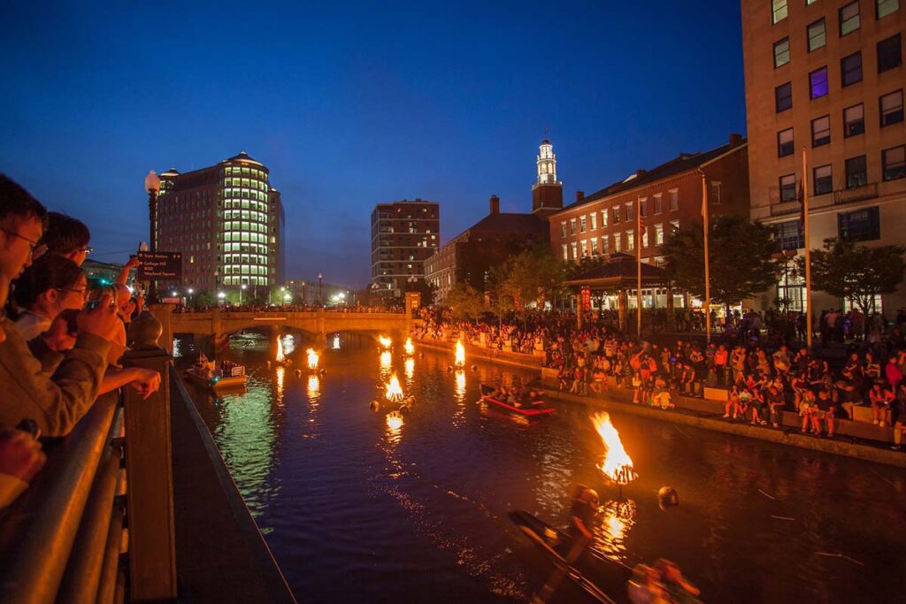 Guest boats pass the lit braziers at WaterFire. Photograph by Erin Cuddigan.